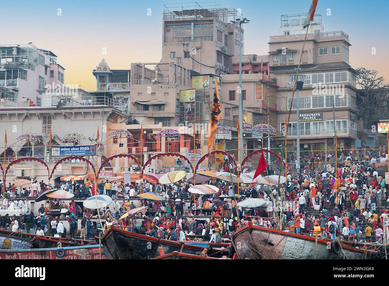 Varanasi, India - February 24, 2024: old  wooden boats at the pier on the border of Rriver Ganges in morning light with many people at the pier and on Stock Photo