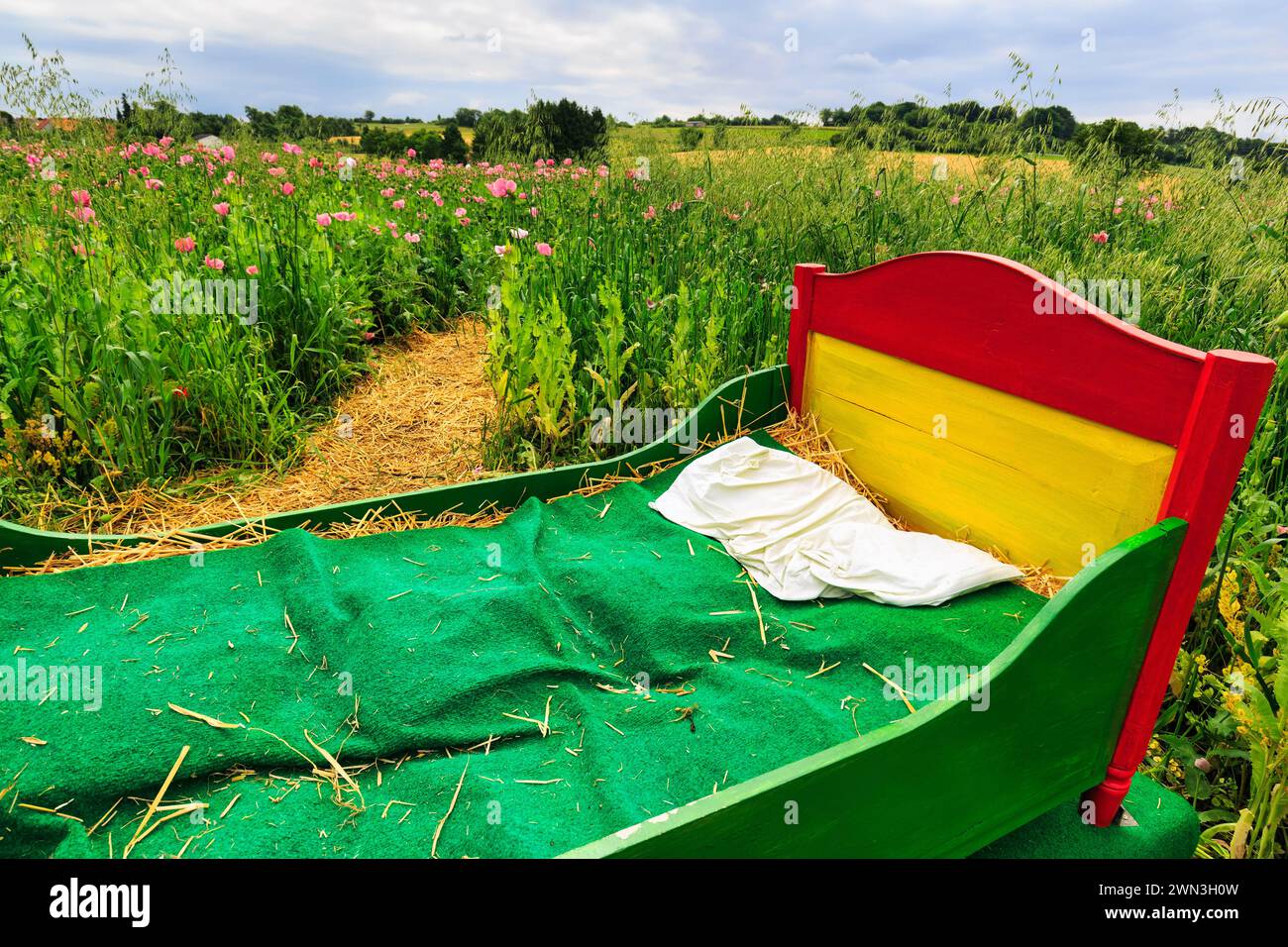 Colourful wooden bed outdoors, mattress made of straw, original hiking trail in the poppy field, symbol of fresh air, taking a break, relaxation Stock Photo