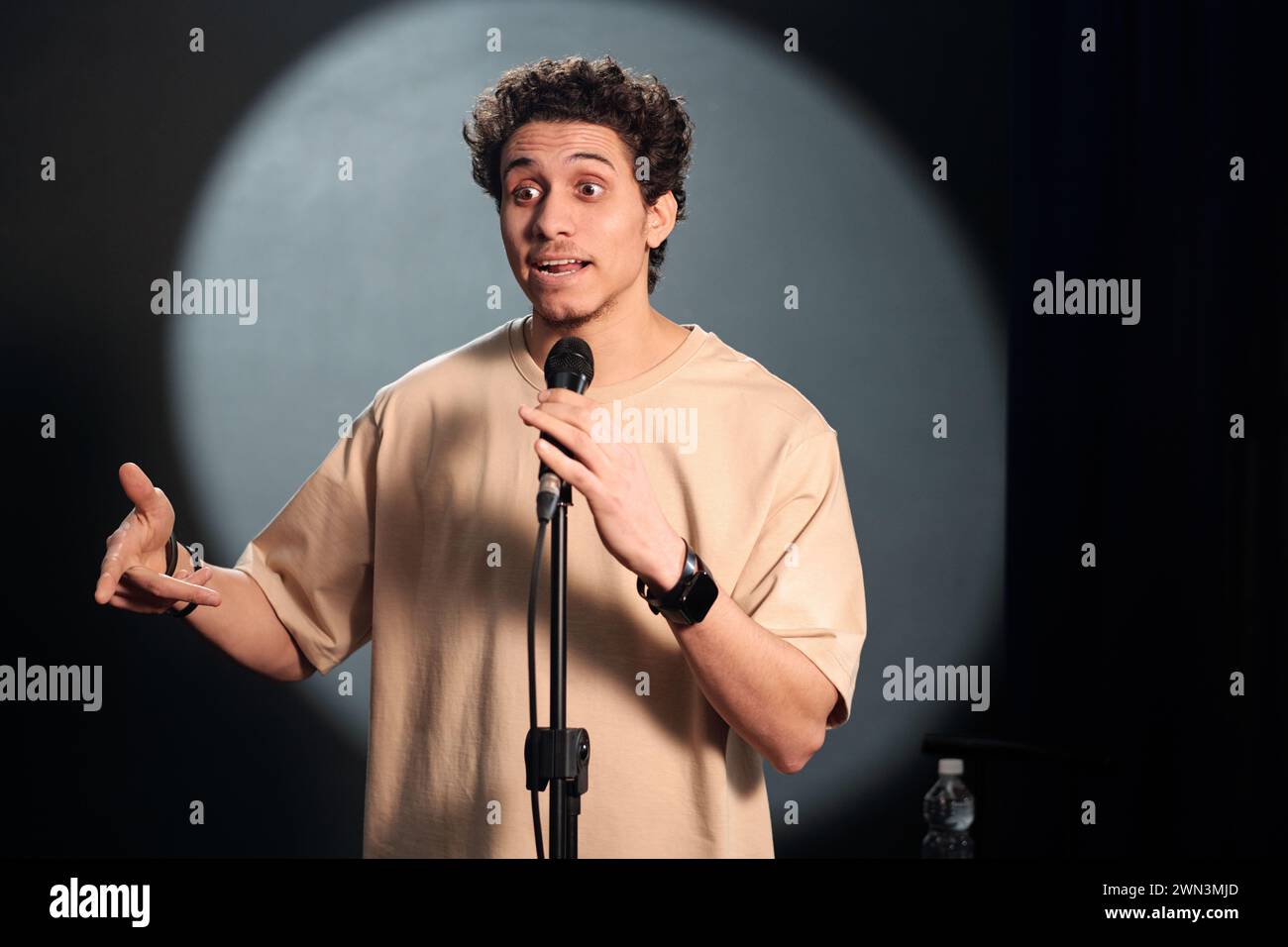 Young comedian of stand up club standing on stage in front of audience ...