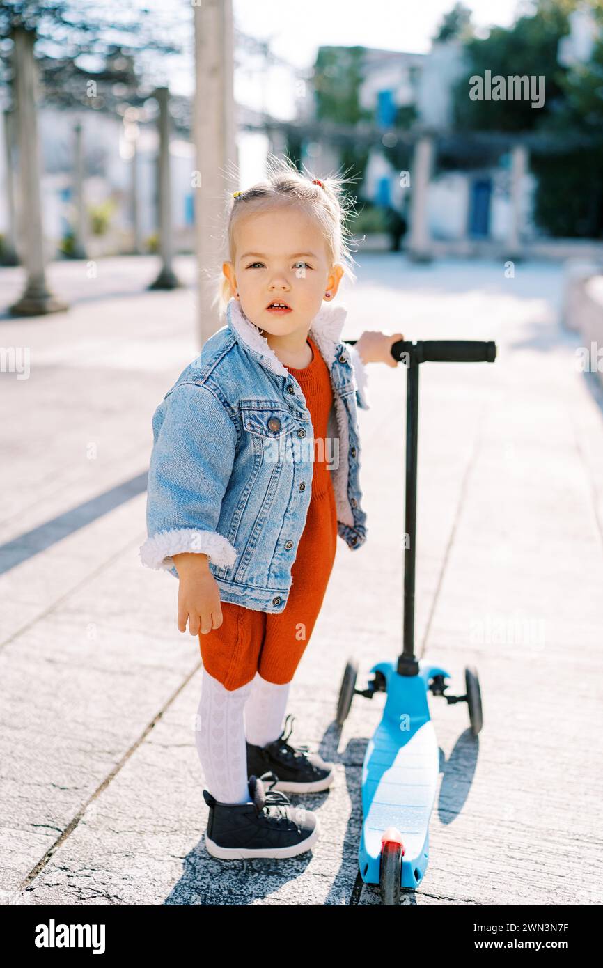 Little girl stands near a threewheeled scooter holding its steering