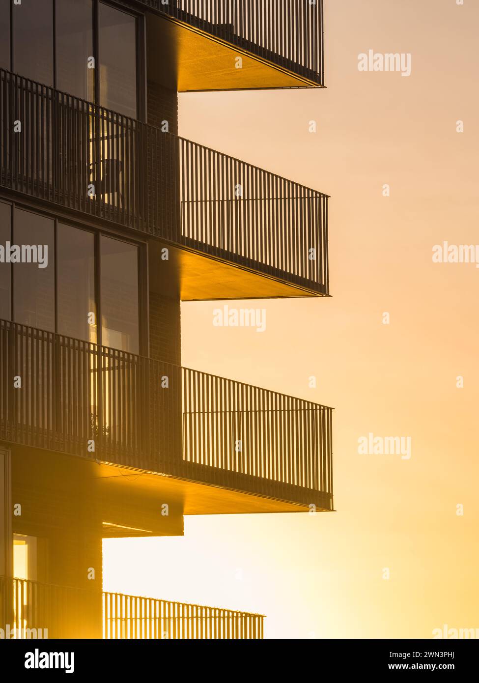 The warm glow of the sunrise bathes the balconies of a contemporary building façade in Gothenburg, creating a serene atmosphere. The silhouettes of th Stock Photo