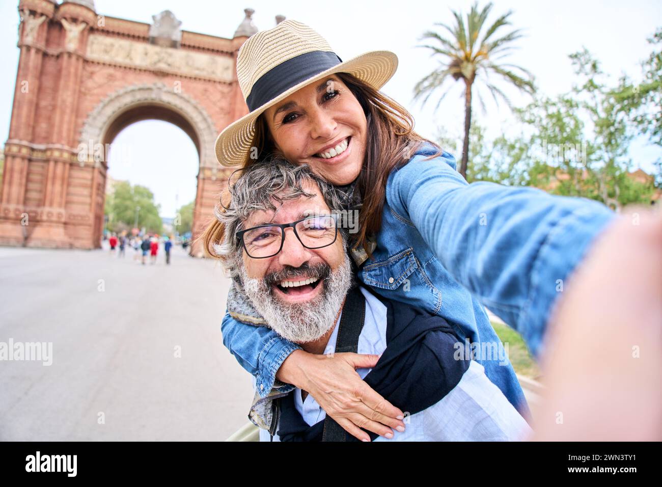 a man is carrying a woman on his back while they take a selfie Stock Photo