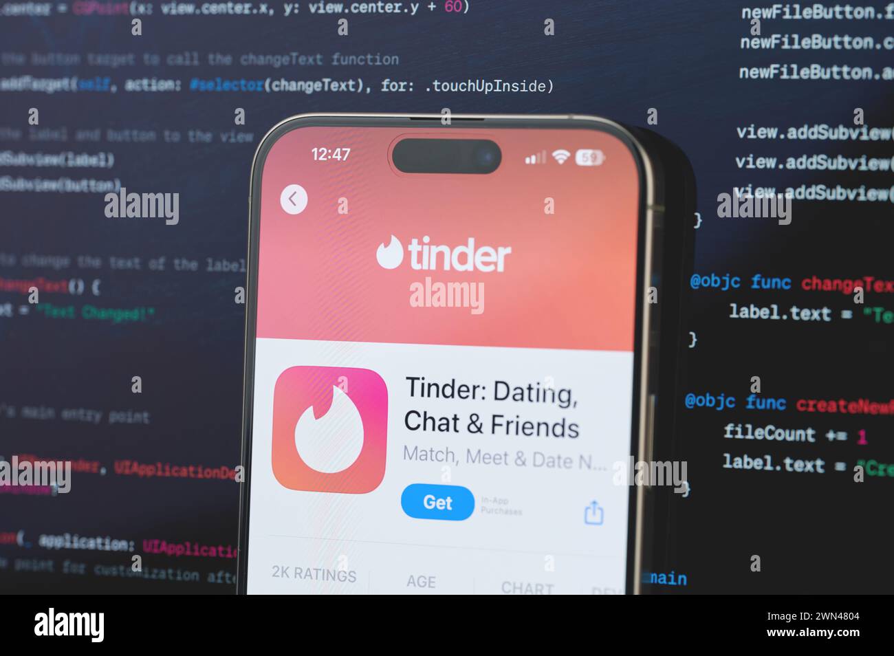 New York, USA - February 23, 2024: Tinder on iphone screen in blurred code programming background Stock Photo