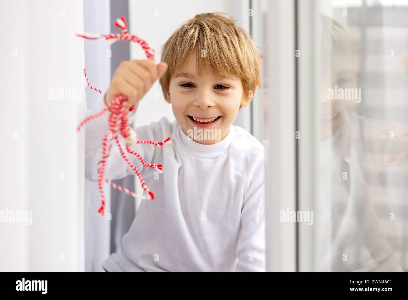 Cute child, blond boy, playing with white and red bracelet, martenitsa Stock Photo