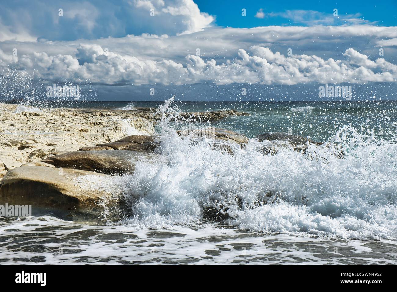 Waves crashing on a rocky coast. Impressive cloudscape with threatening thunderclouds and blue sky. South coast of Cyprus. Stock Photo