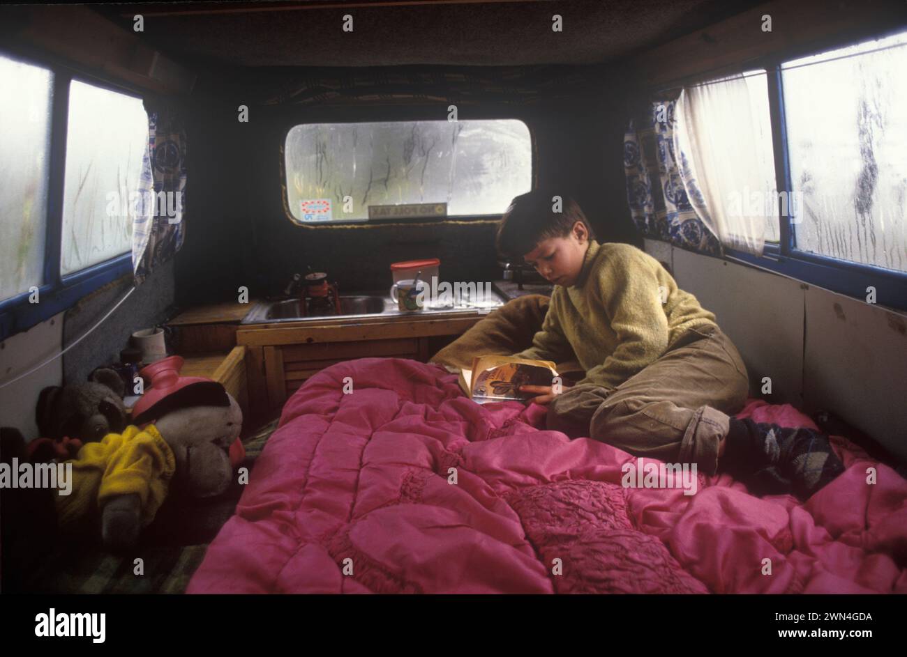 Off Grid Living 1980s UK. Child, young boy in his father van reading a book.(Watership Down)  Kevin Oubridge lived with his family in Tipi Valley a Welsh hippy community that was home to around 120 eco friendly free spirits. Llandeilo, Wales 1985 HOMER SYKES Stock Photo