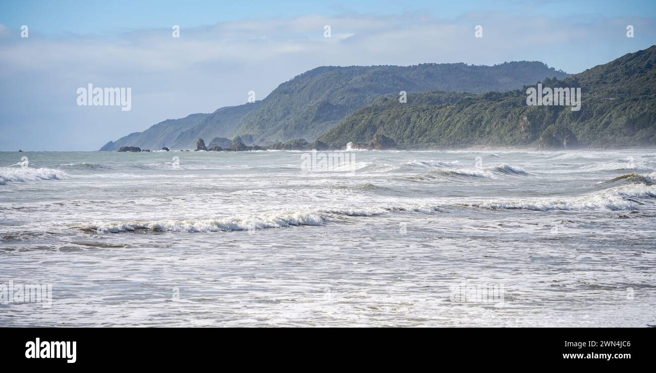 Rough exotic coastal landscape with big waves and rainforest vegetation on a sunny day, New Zealand Stock Photo