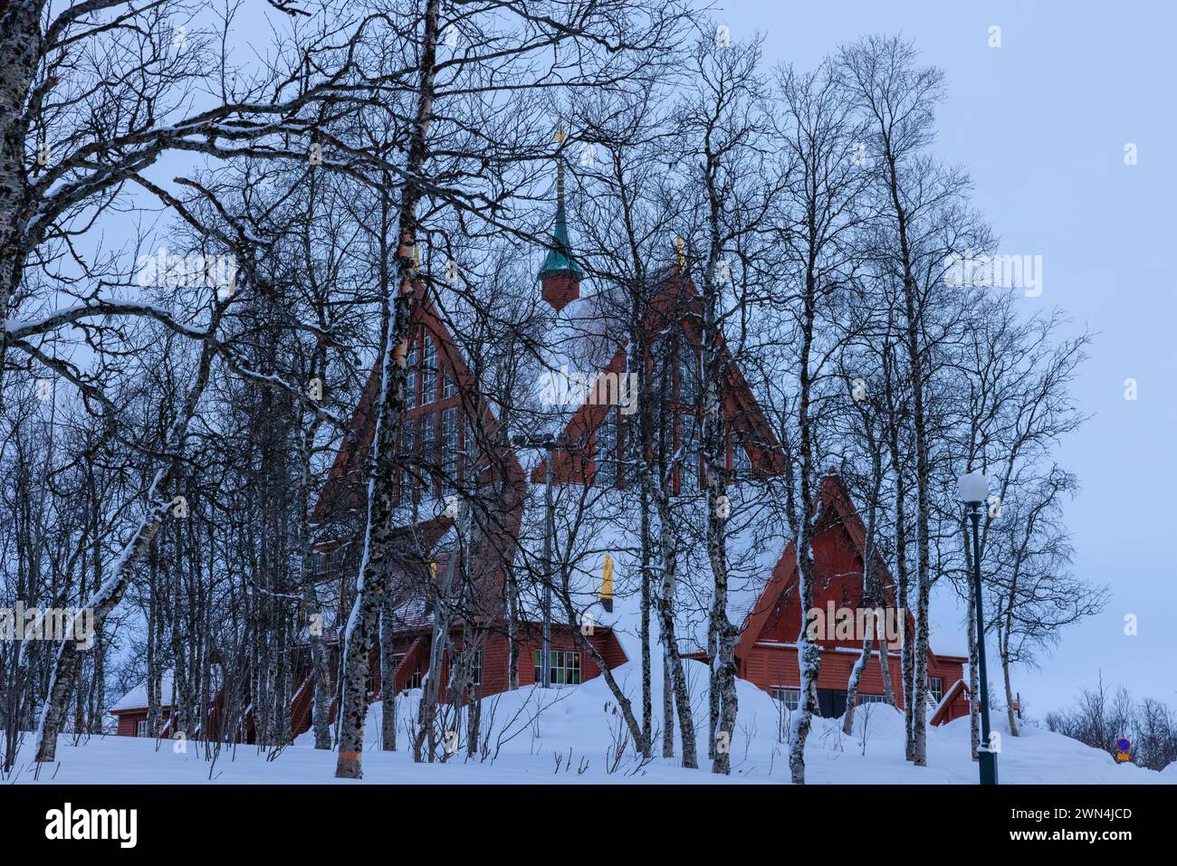 brown wooden gables and snowy roof of kiruna church seen through a small copse of dark wooden trees Stock Photo