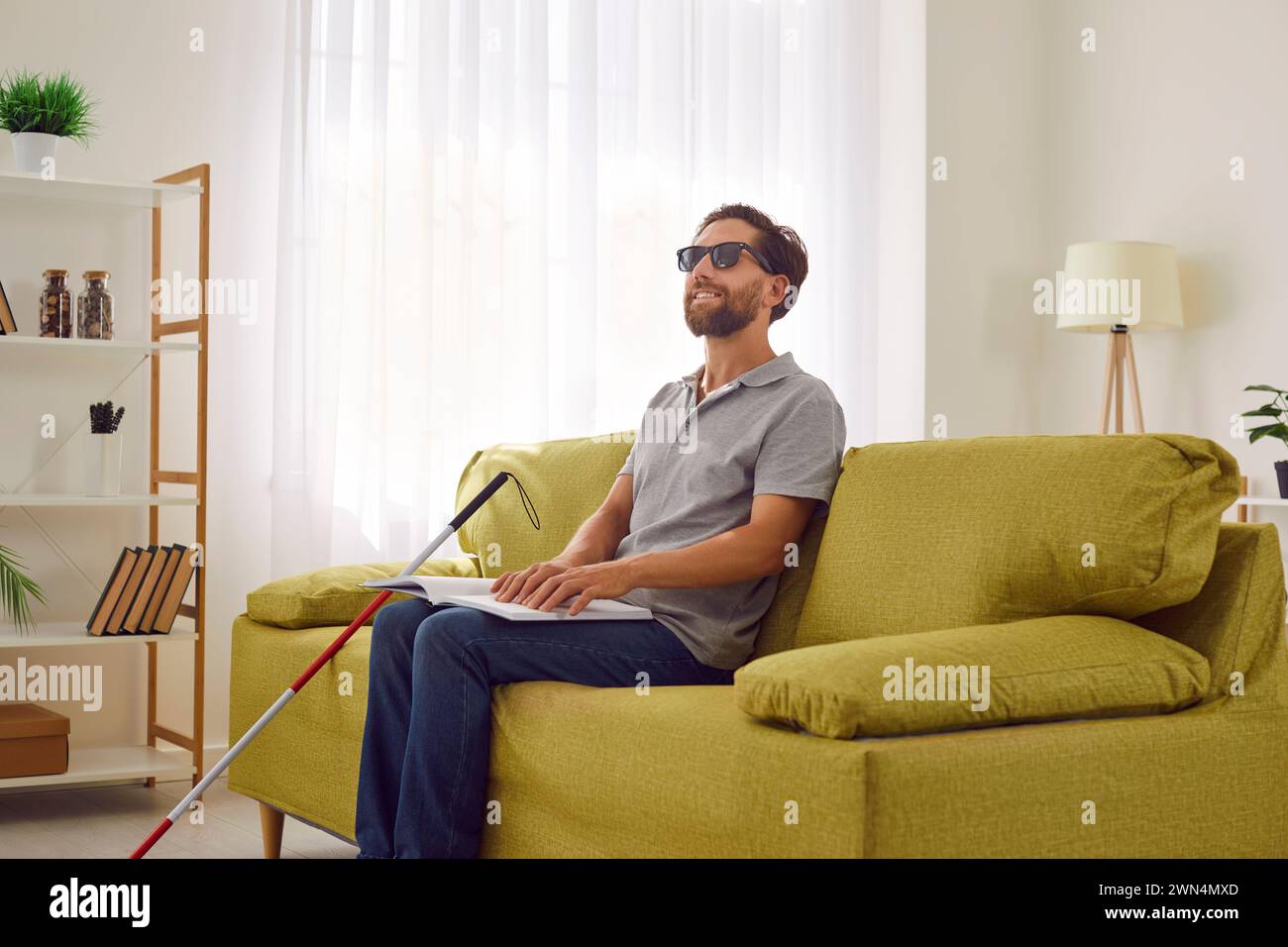 Blind Man Smiles While Reading Braille Book on Sofa Stock Photo