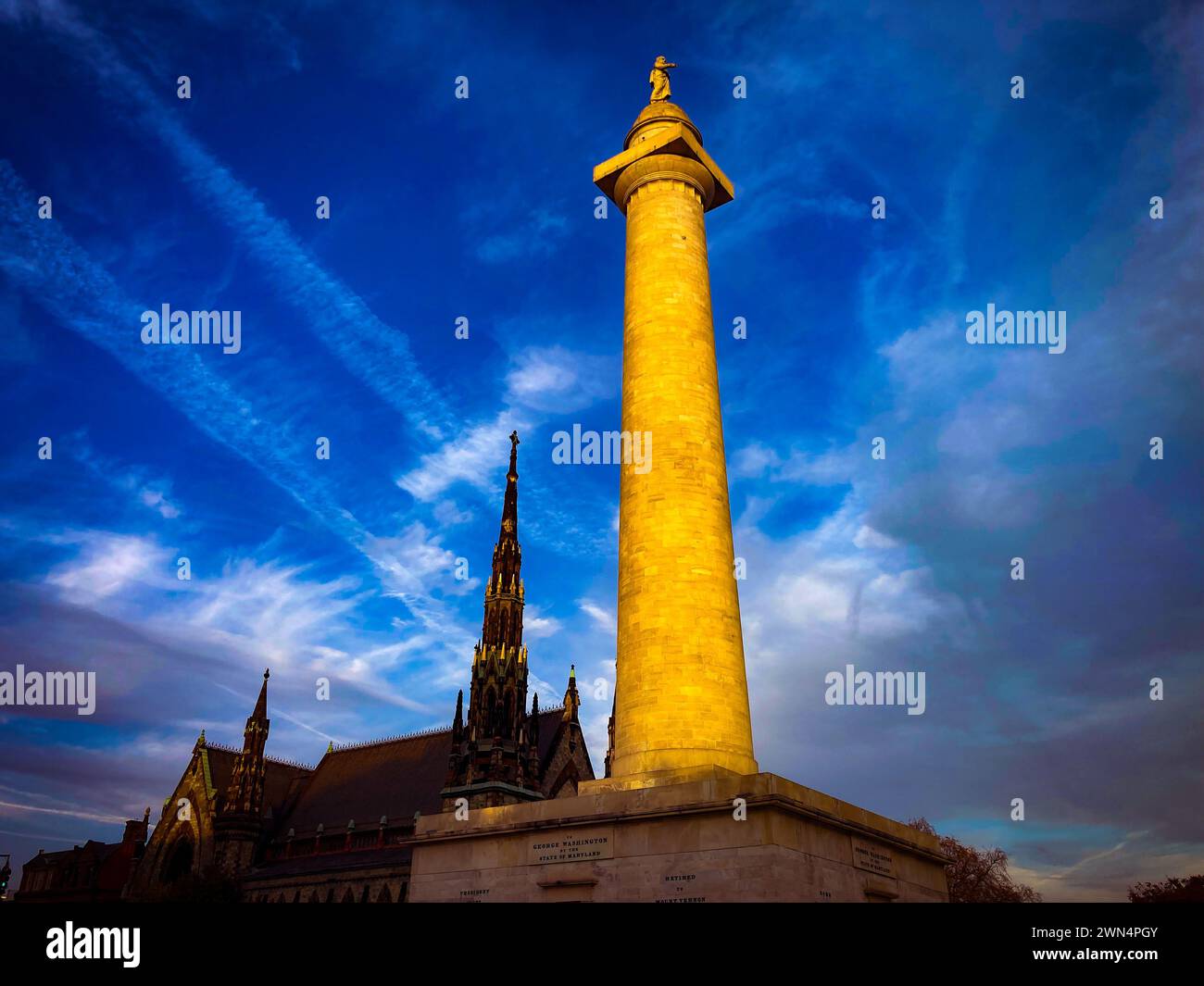 Washington Monument and gothic church in Mount Vernon in Baltimore Maryland with blue skies and white clouds Stock Photo