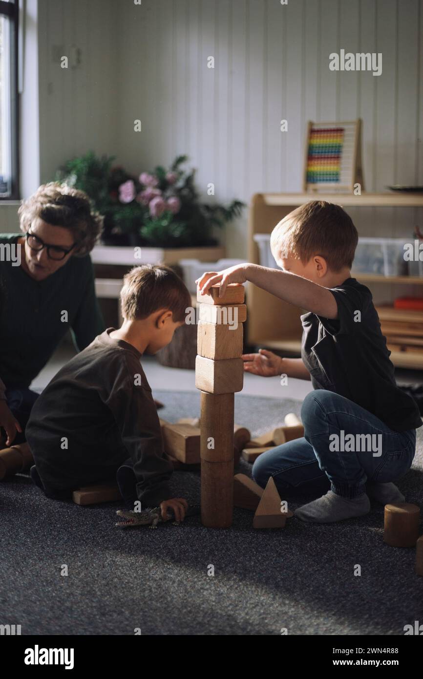 Schoolboys playing with toy blocks with female teacher in classroom at kindergarten Stock Photo