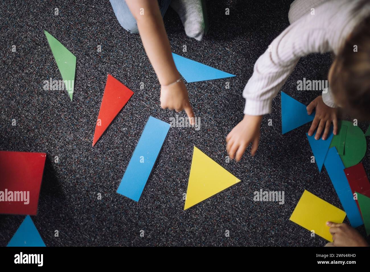 Directly above view of kids playing with geometric shapes on floor in classroom at kindergarten Stock Photo