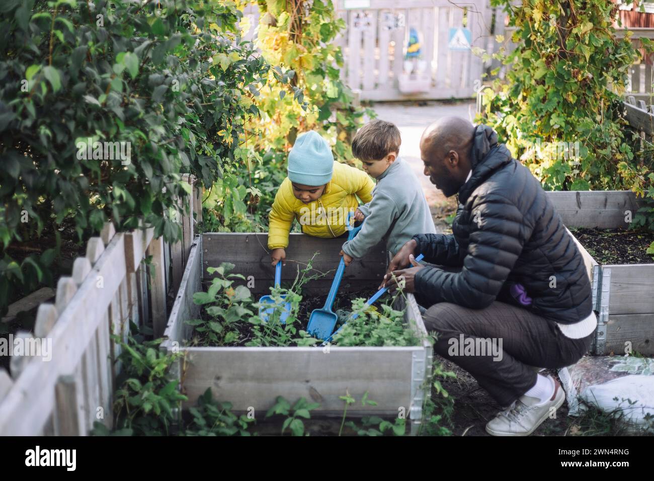 Side view of male teacher crouching near kids doing gardening at garden Stock Photo