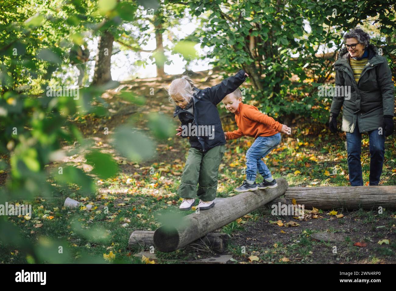 Female teacher looking at children balancing on wooden logs while ...