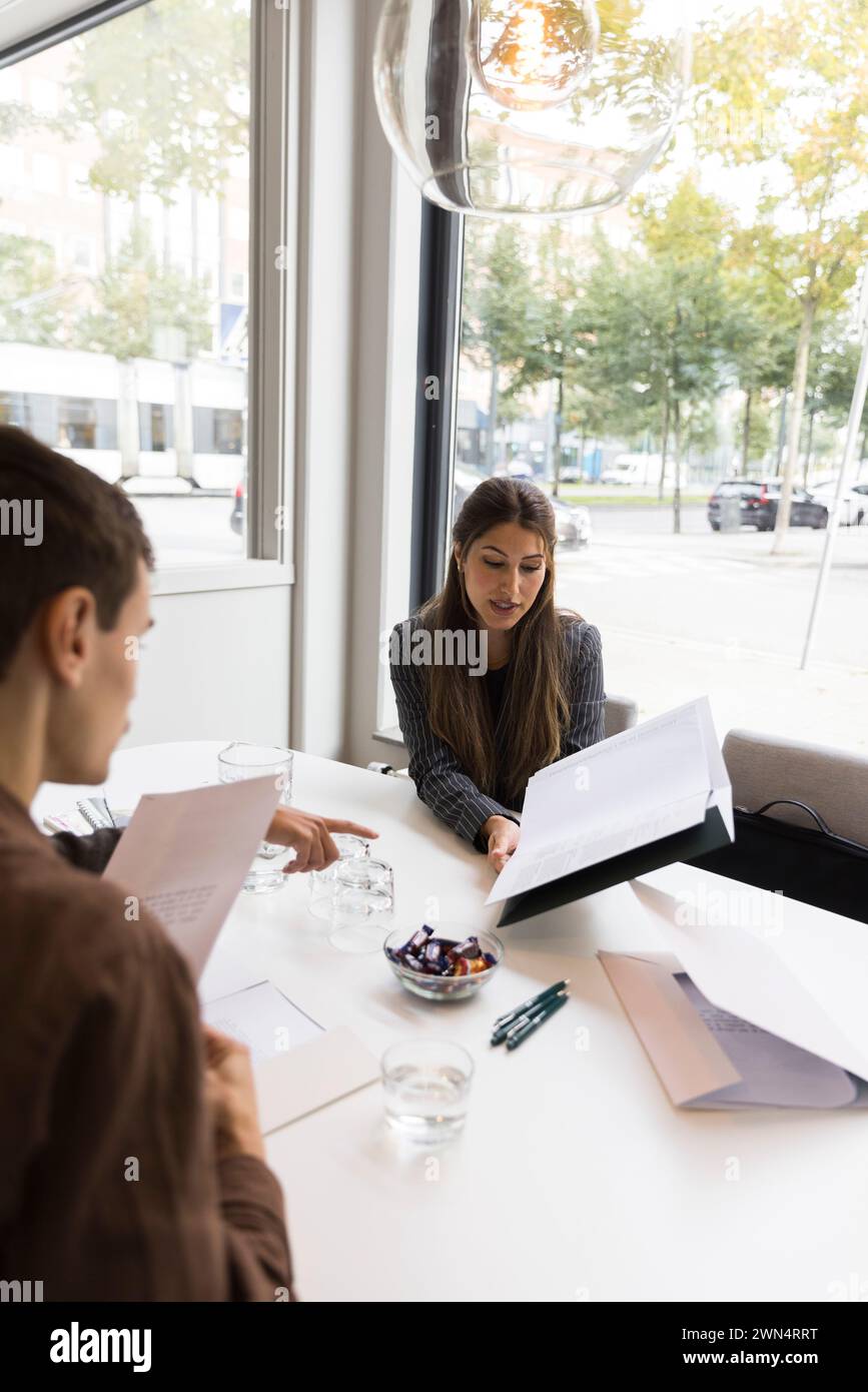 Female real estate agent explaining floor plan to customers in office Stock Photo