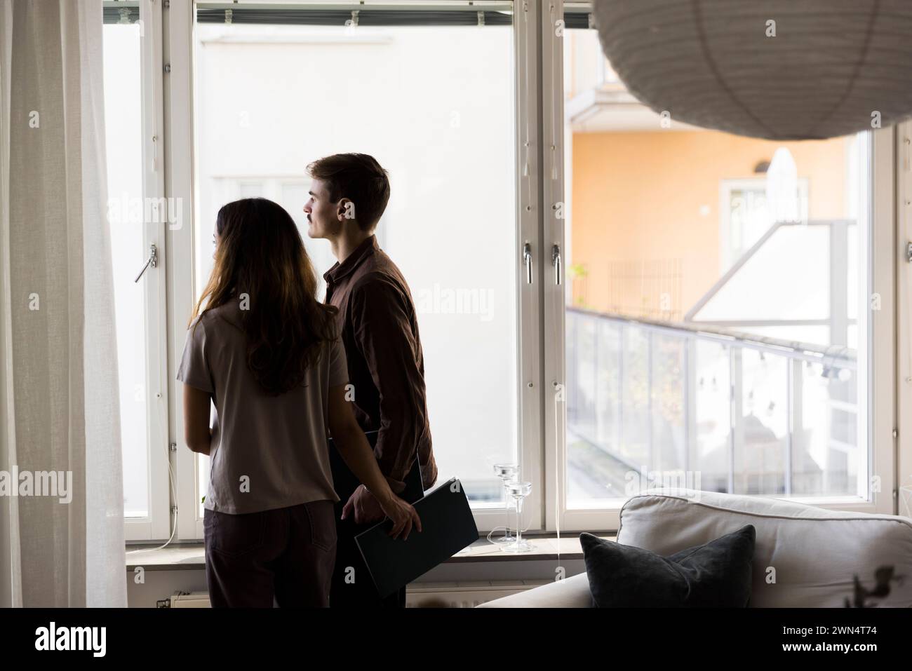 Multiracial couple looking through window while standing at new home Stock Photo