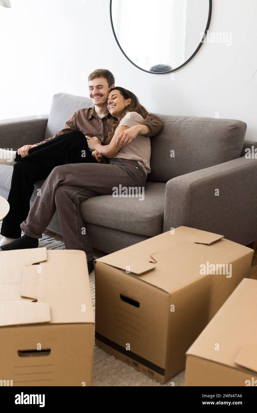 Happy couple embracing while sitting on sofa by cardboard boxes at home Stock Photo