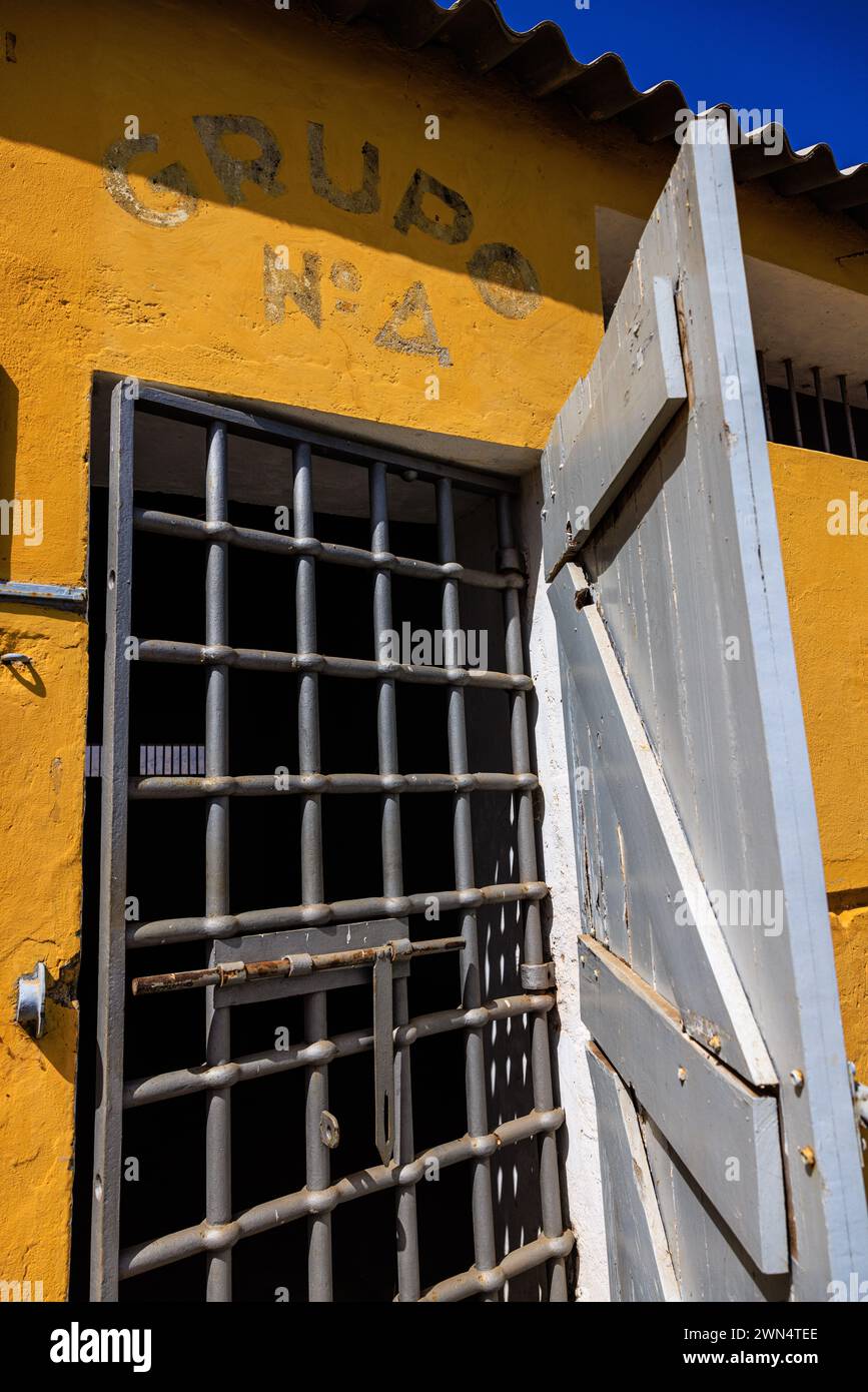 an iron barred gate and white wooden door secure the doorway to a cell at tarrafel concentration camp for portuguese dissidents in Cabo Verde Stock Photo