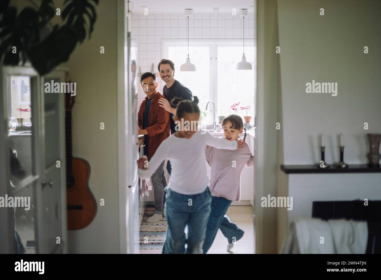 Gay couple looking at daughters running while playing at home Stock Photo