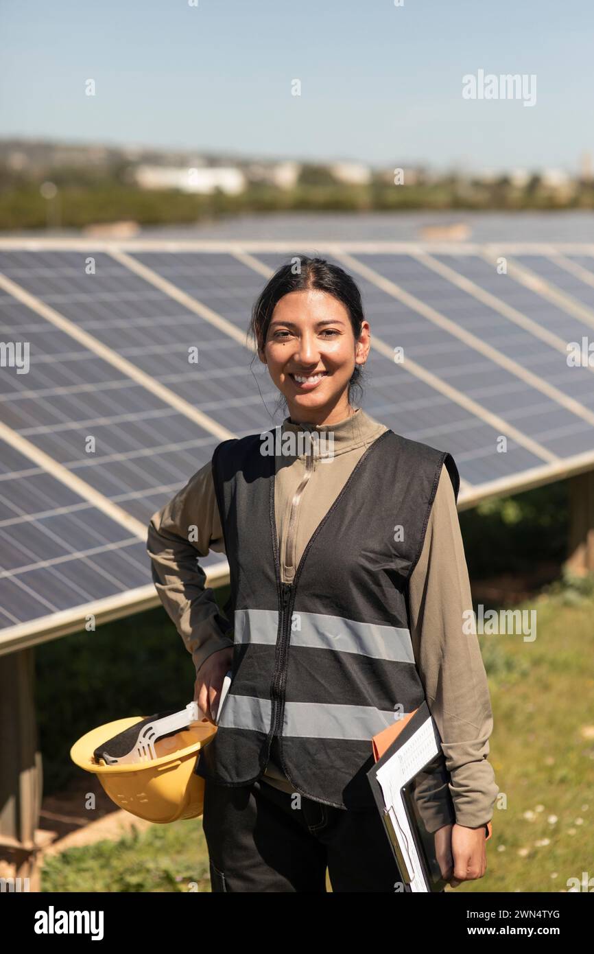 Portrait of confident female engineer standing with hand on hip near solar panels in field Stock Photo