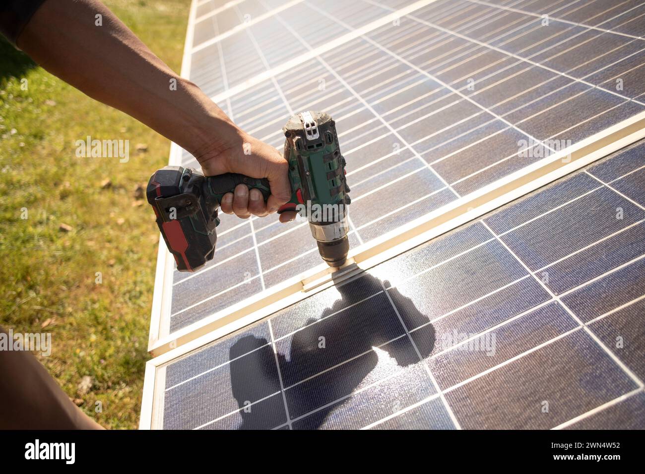 Hand of male engineer using drill on solar panels while working at power station Stock Photo