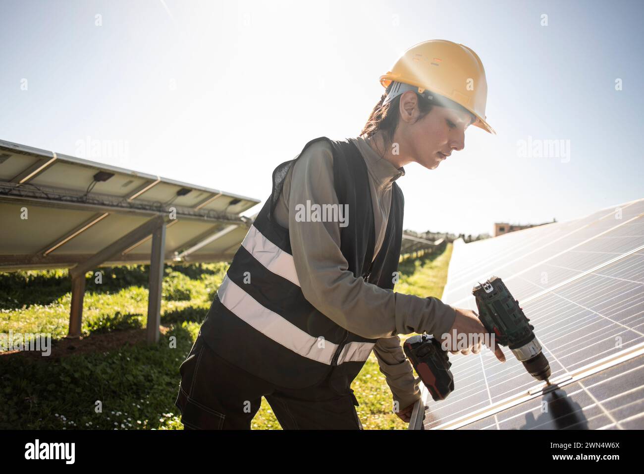 Female engineer using drill while working near solar panels at power station Stock Photo