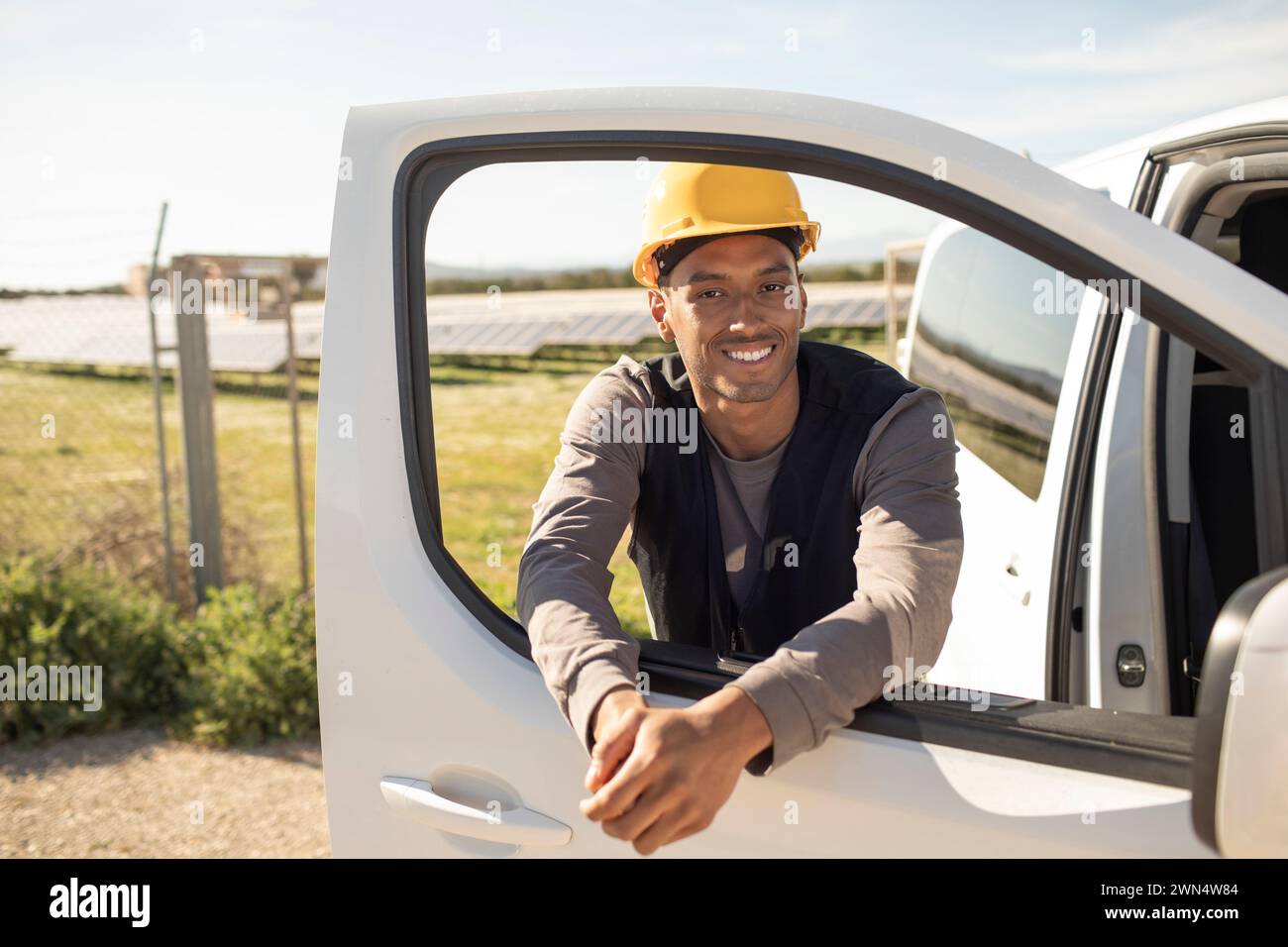 Portrait of young smiling male engineer leaning on van door at power station Stock Photo