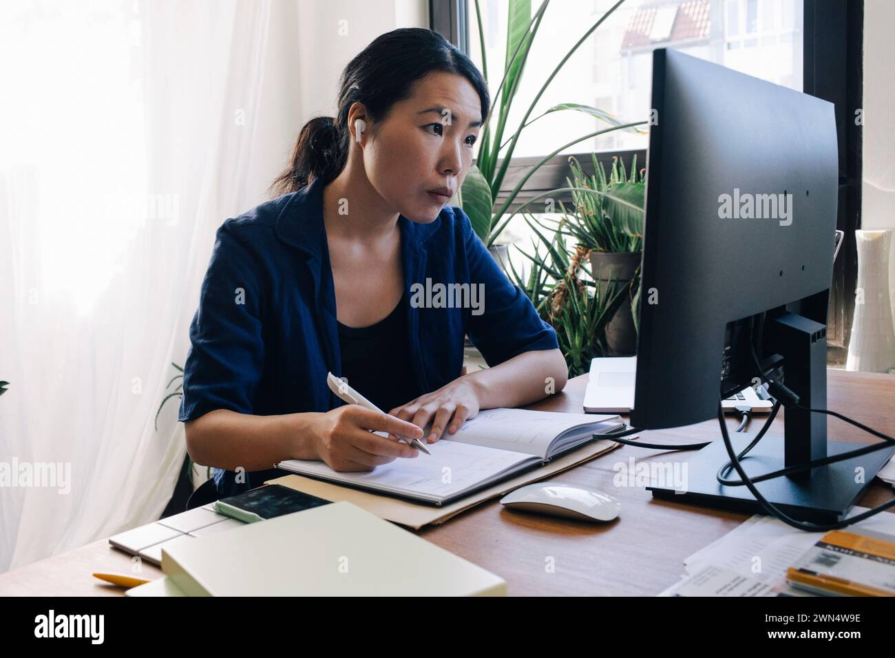 Confident female architect with diary looking at computer monitor on desk in home office Stock Photo