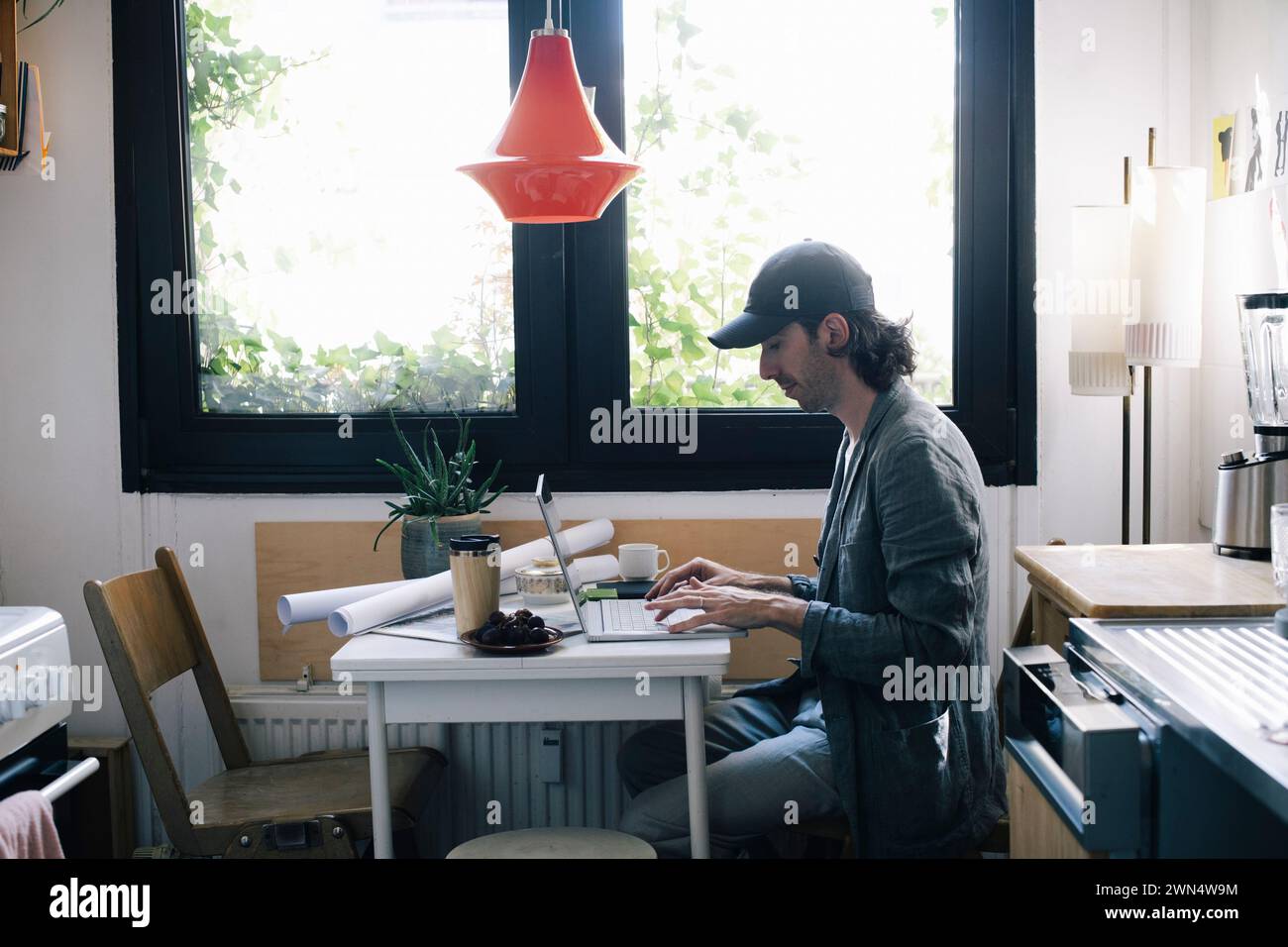 Side view of male architect using laptop at desk in home office Stock Photo