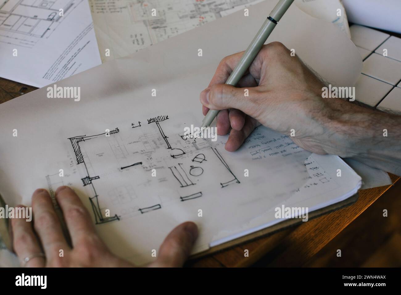 Cropped hands of male architect sketching blueprint on paper at desk in home office Stock Photo