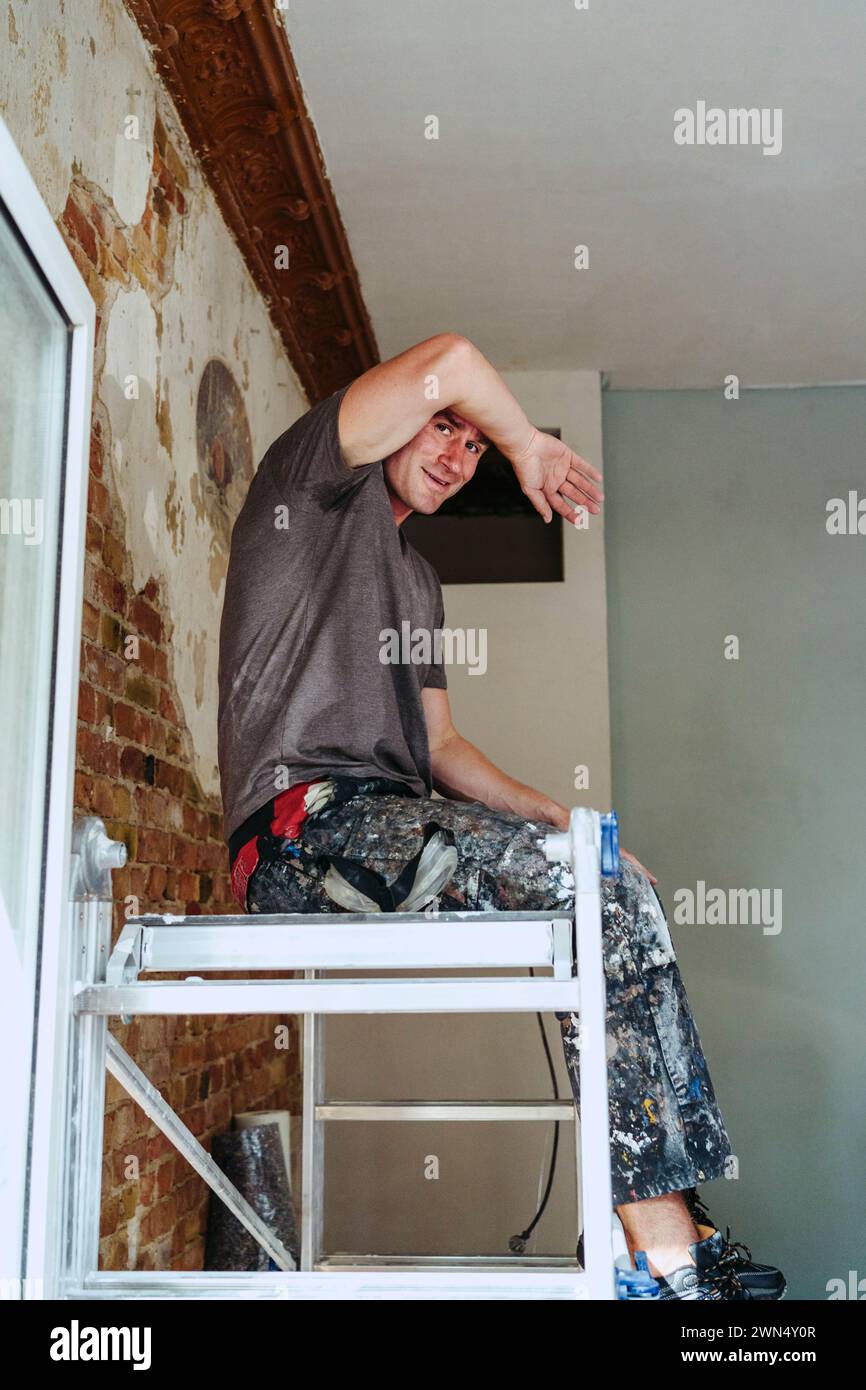 Smiling male worker sitting on ladder in break at site Stock Photo