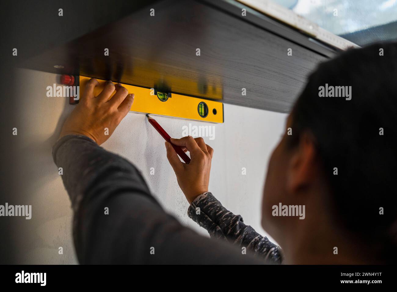 Female carpenter using bubble level and marking on wall with pencil Stock Photo
