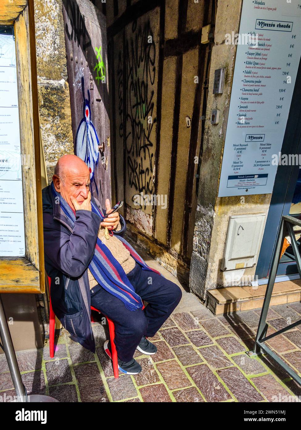 Elderly man with smartphone and worry beads sitting outside middle eastern restaurant - Tours, Indre-et-Loire (37), France. Stock Photo