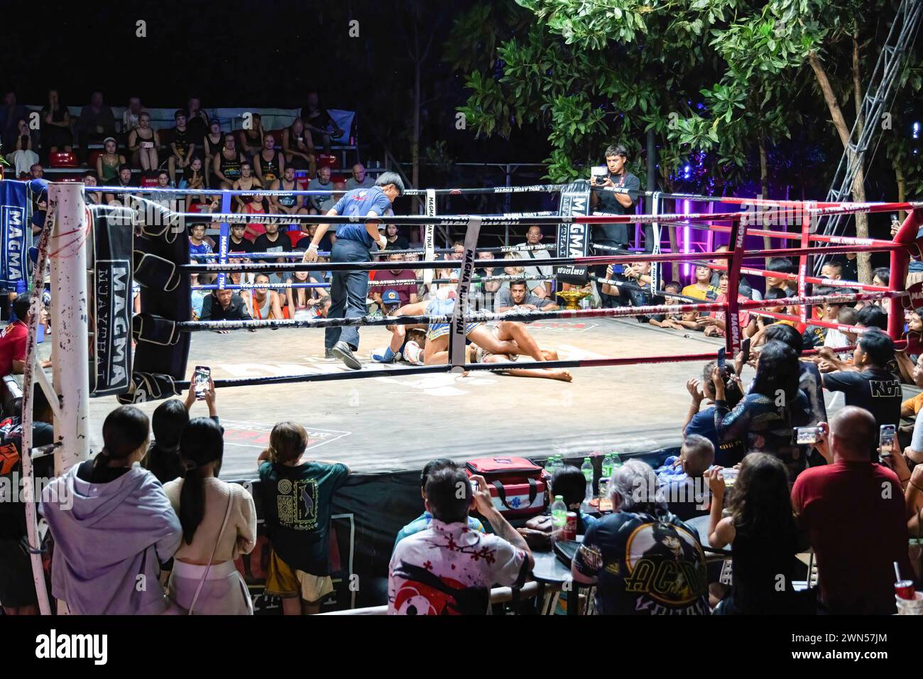 Koh Chang, Thailand. 24th Feb, 2024. The referee is seen standing above the boxers Petch Morakot and Angor Tamin while they fight, at the Muay Thai Fights weekly show in Koh Chang. Koh Chang Fight organizes weekly Muay Thai fights in an open-air stadium, with a show composed of six fights presented in English, drawing over a hundred tourists each week who stay on Koh Chang Island. The last of six fights: Boxer Petch Morakot defeated Angor Tamin. Credit: SOPA Images Limited/Alamy Live News Stock Photo