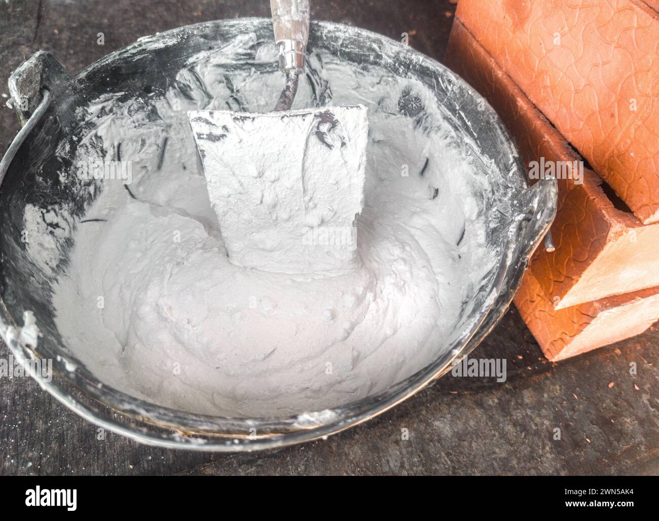 Bucket full white adhesive mortar ready for applicate. Bricks as background Stock Photo