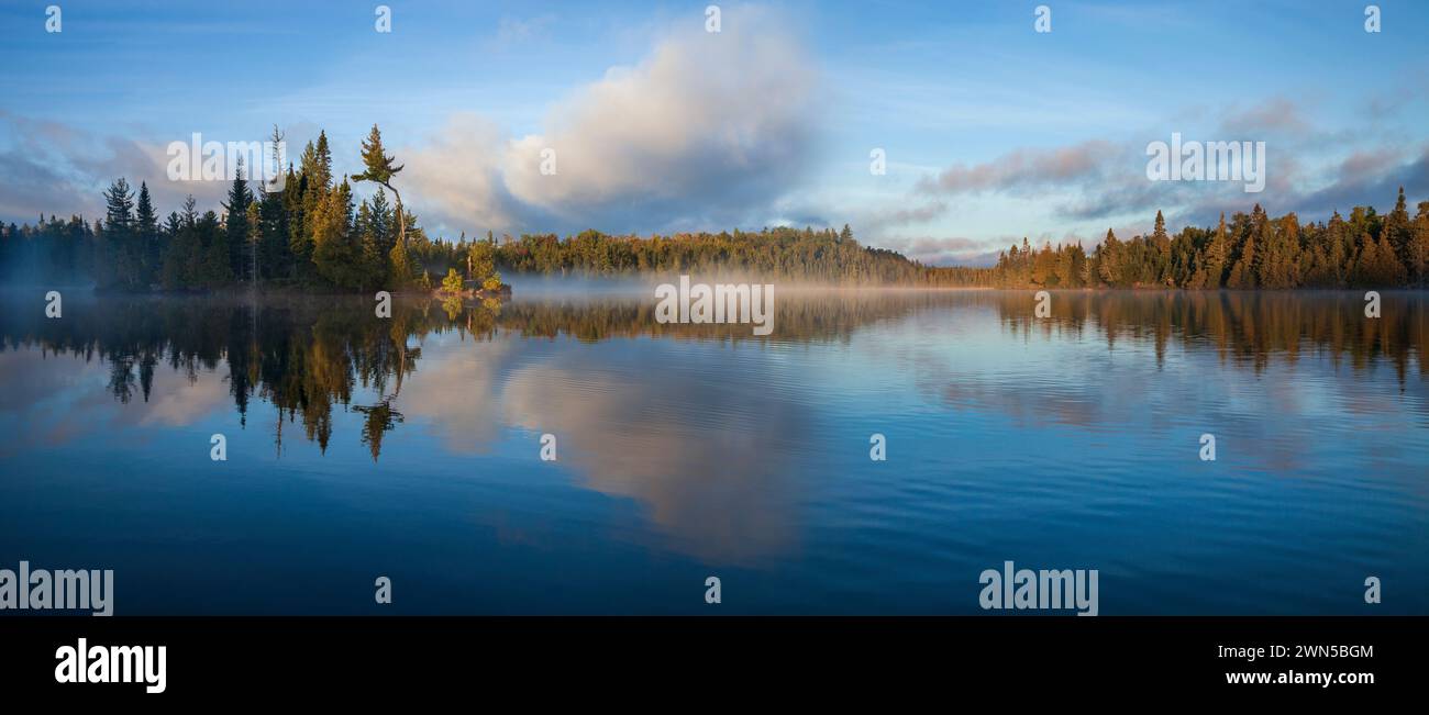 Panorama of blue lake in northern Minnesota with an island and pines on a foggy September morning Stock Photo