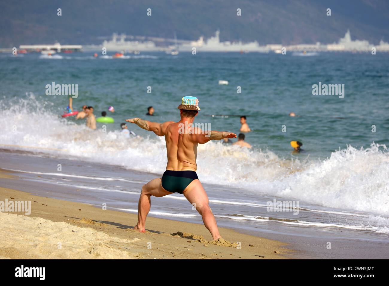 Yoga on the beach, muscular man stands on sea waves background. Balance with nature, fitness and exercise at vacation Stock Photo