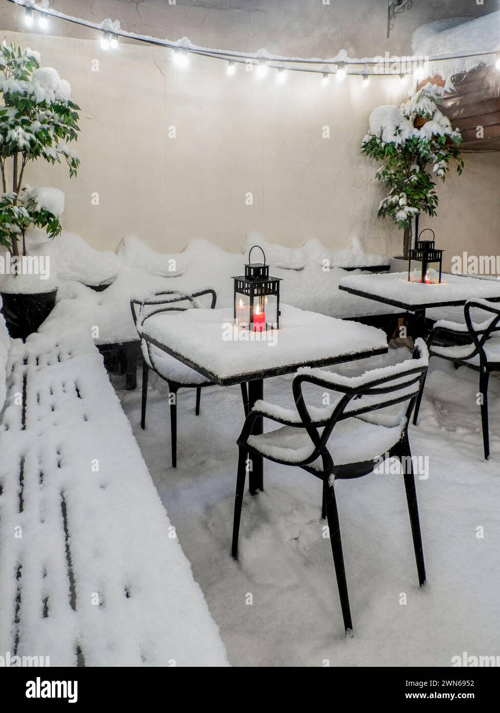 Tables and chairs covered in fresh snow at winter time, burning red candle on the table covered with fresh snow Stock Photo