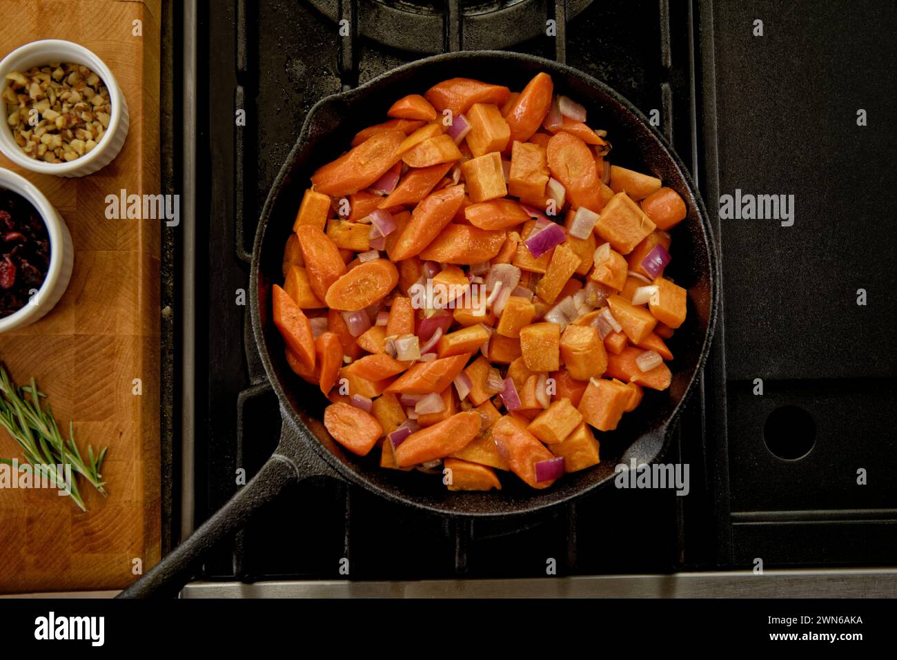 A top view of a cast iron pan with chopped carrots on a stove beside ...