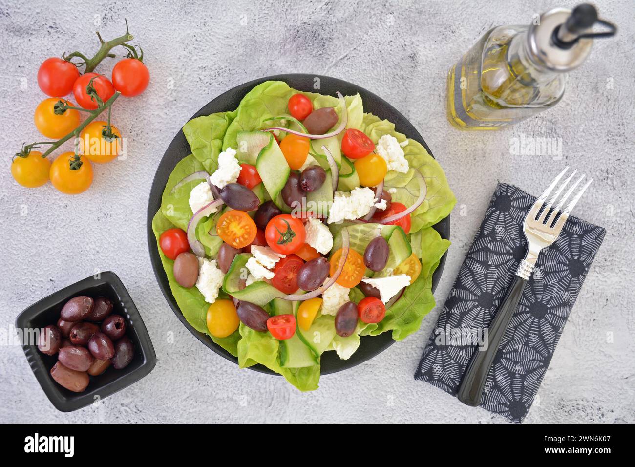 Healthy nutritious Greek salad with cherry tomatoes,Kalamata olives,feta cheese red onion slices and cucumber ribbons on stone background in flat lay Stock Photo