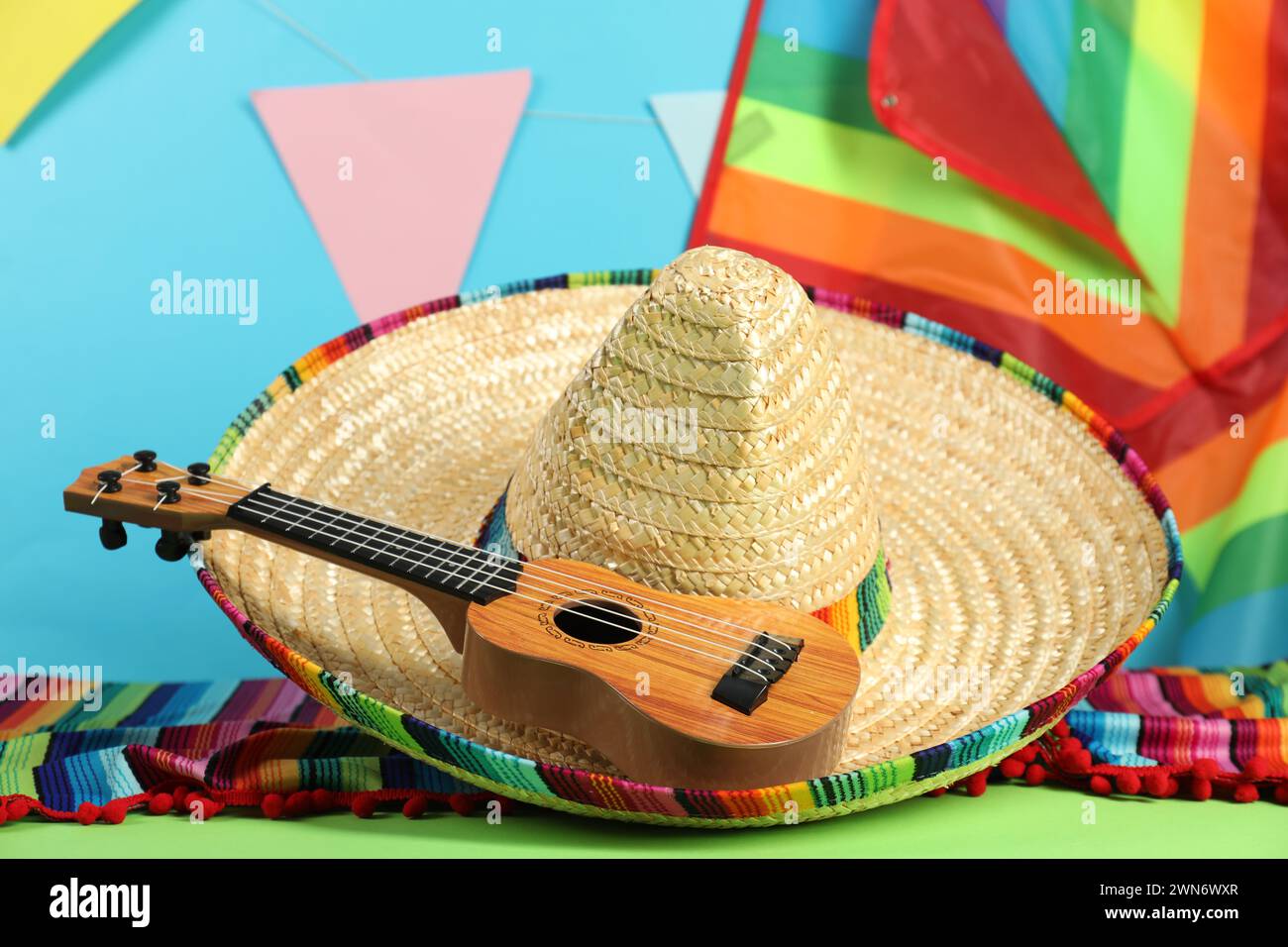 Mexican sombrero hat, poncho and ukulele on green table, closeup Stock Photo