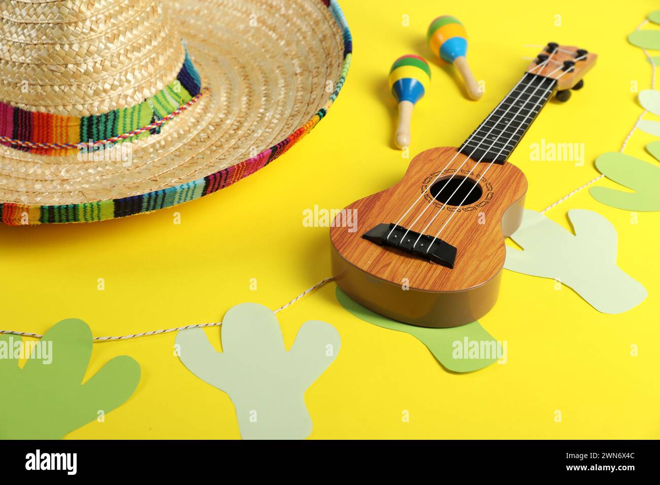 Mexican sombrero hat, maracas, ukulele and garland on yellow background