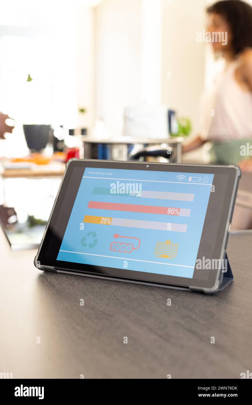 Tablet with smart home app on screen sits on kitchen counter; young biracial woman in background Stock Photo