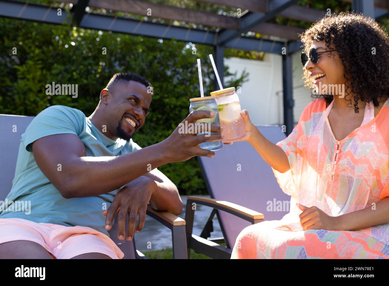 Casually dressed duo enjoys sunny outdoor drinks, sharing joy. Stock Photo
