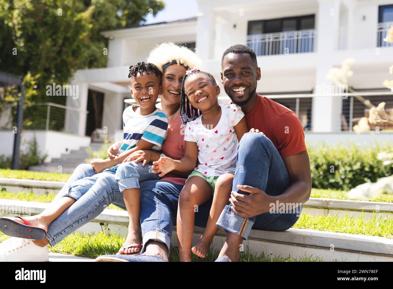 African American man and young biracial woman sit with a boy and a girl, all smiling Stock Photo