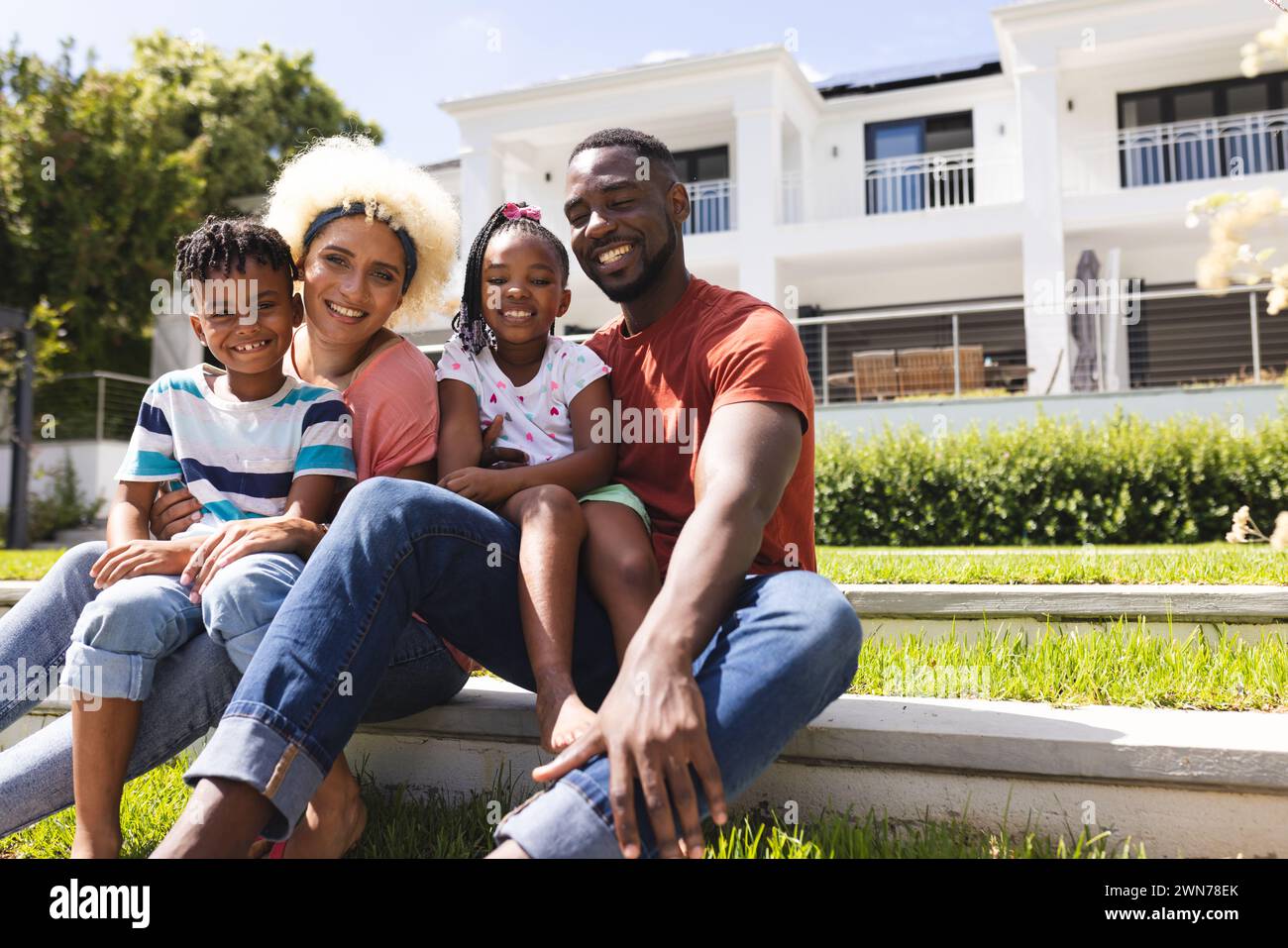 Diverse family enjoys time together outdoors, with a modern home in the background Stock Photo