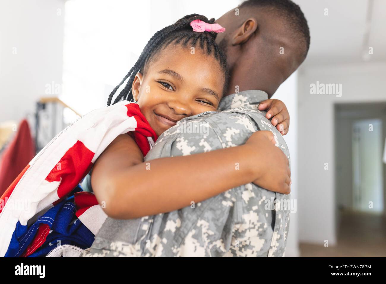 African American girl embraces a soldier, her smile radiates joy, with an American flag Stock Photo
