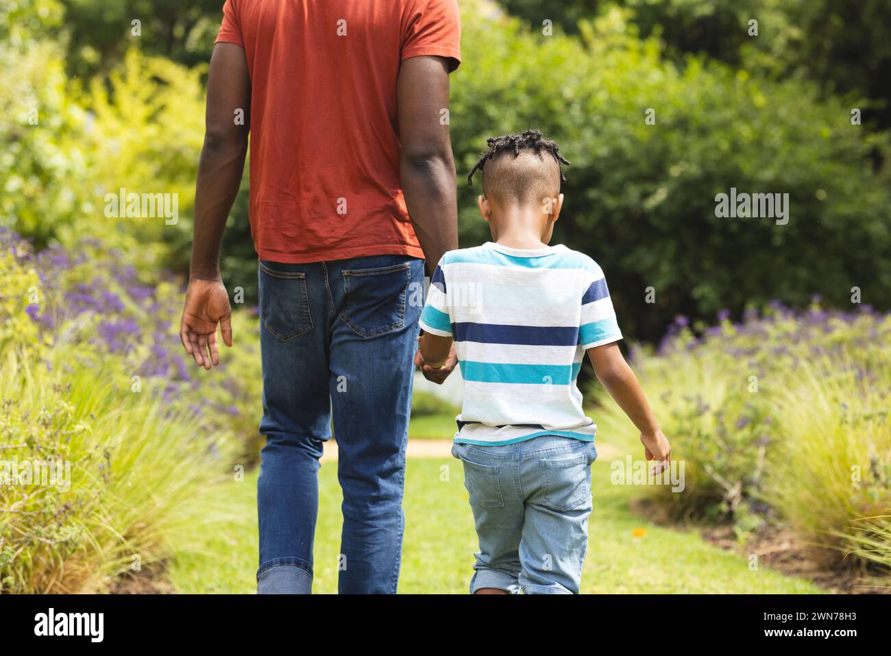 African American father and son walk hand in hand through a lush garden Stock Photo