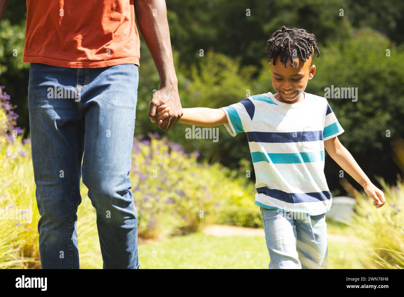African American father and son walk hand in hand in a sunny park Stock Photo