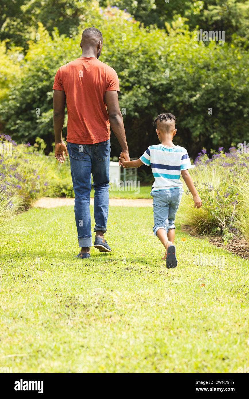 African American father and son walk hand in hand in a lush garden Stock Photo